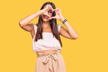 Gündelik kıyafetler ve gözlük takan genç İspanyol kadın kalp şeklinde el ve parmaklarıyla gülümsüyor ve tabelanın içinden bakıyor. 