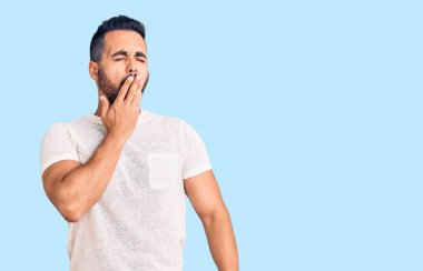 Gündelik kıyafetler giyen genç İspanyol adam ağzıyla ağzını kapatmaktan sıkılmış. Huzursuz ve uykulu.. 