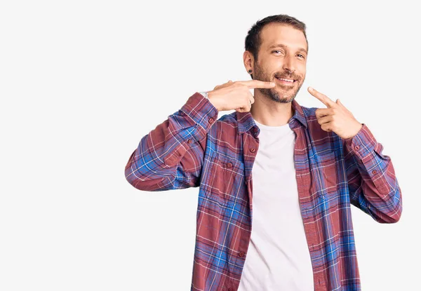 Gündelik kıyafetler giyen, neşeli gülümseyen, parmaklarıyla ve ağzıyla işaret eden genç yakışıklı bir adam. diş sağlığı kavramı. 