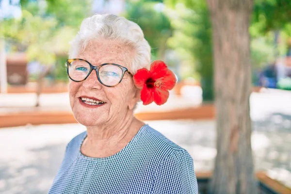 Yaşlı yaşlı, gri saçlı, dışarıda mutlu gülümseyen, dekoratif bir çiçek takan yaşlı kadın.