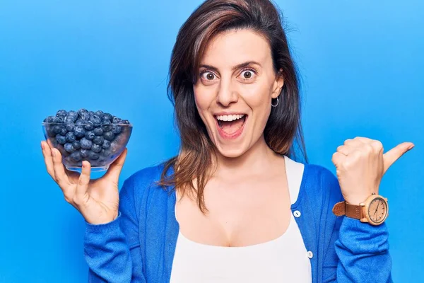 Elinde yaban mersini tutan genç ve güzel bir kadın başparmağını yana uzatıyor ve ağzı açık gülümsüyor. 