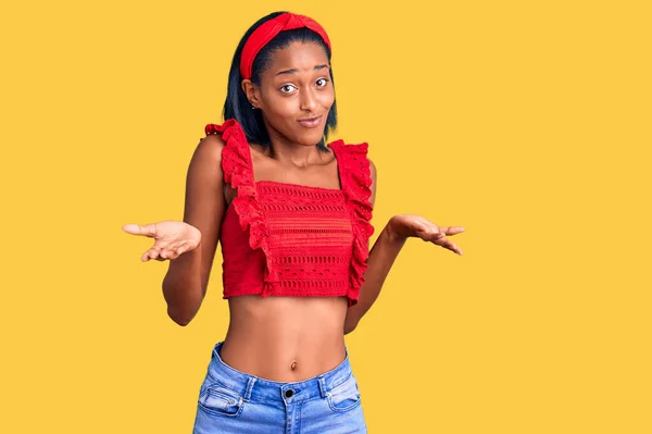 年轻的非洲裔美国女人穿着休闲的夏装 毫无头绪 满脸困惑 手臂和双手高举 怀疑概念 — 图库照片