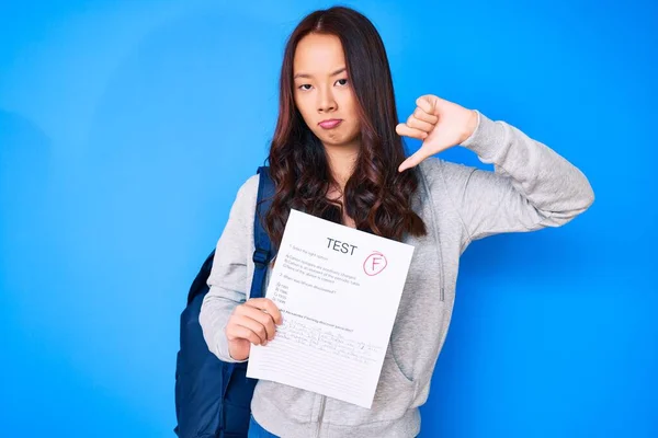 Young beautiful chinese girl showing a failed exam with angry face, negative sign showing dislike with thumbs down, rejection concept