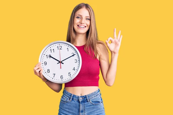 Joven Hermosa Mujer Rubia Sosteniendo Gran Reloj Haciendo Signo Con —  Fotos de Stock