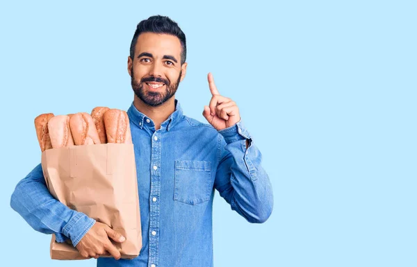 Young Hispanic Man Holding Bag Bread Surprised Idea Question Pointing — Stock Photo, Image