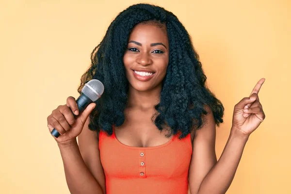 Hermosa Mujer Africana Cantando Canción Usando Micrófono Sonriendo Feliz Señalando —  Fotos de Stock