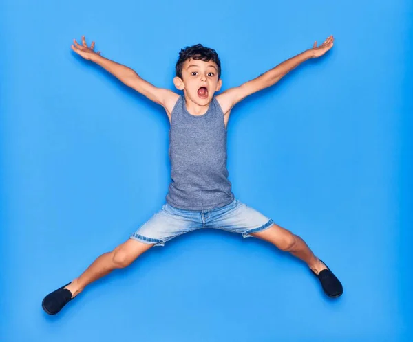 愛らしい子供はカジュアルな服を着ています 孤立した青の背景の上に腕を持つジャンプ — ストック写真