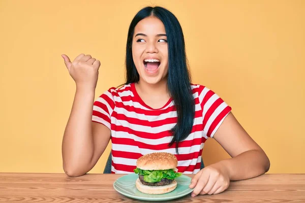 Fiatal Ázsiai Lány Eszik Egy Ízletes Klasszikus Hamburger Mutató Hüvelykujj — Stock Fotó