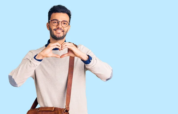 Young handsome hispanic man wearing leather bag smiling in love showing heart symbol and shape with hands. romantic concept.