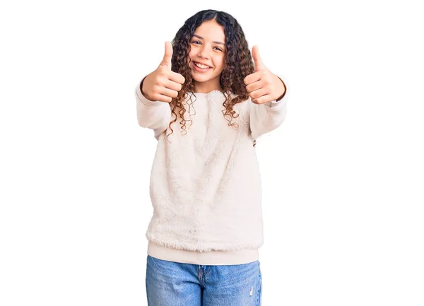 カジュアルな服を着て巻き毛の美しい子供の女の子は 手で肯定的なジェスチャーを行うことを承認し 親指を笑顔と成功のために幸せ 勝者のジェスチャー — ストック写真
