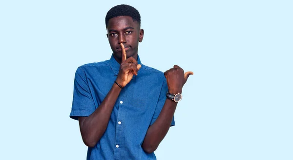 若いアフリカ系アメリカ人の男性がカジュアルな服を着て 唇に手で側に指して指で静かになるように求めている 沈黙と秘密の概念 — ストック写真