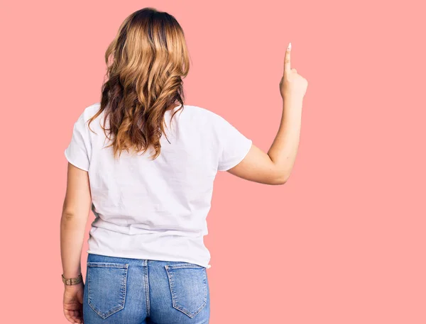 年轻美丽的高加索女人 身穿休闲的白色T恤 背对着身体 手指头指向前方 — 图库照片