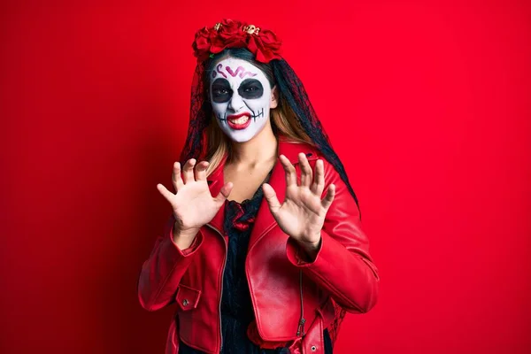 Woman wearing day of the dead costume over red disgusted expression, displeased and fearful doing disgust face because aversion reaction. with hands raised