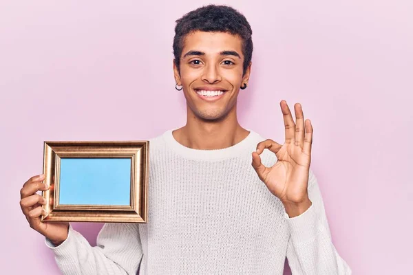 Молодой Африканский Американец Держащий Пустую Рамку Делает Знак Пальцами Улыбаясь — стоковое фото