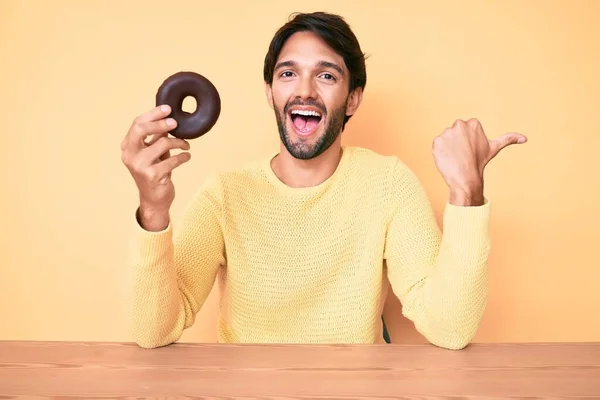 Bonito Hispânico Homem Segurando Donut Apontando Polegar Até Lado Sorrindo — Fotografia de Stock