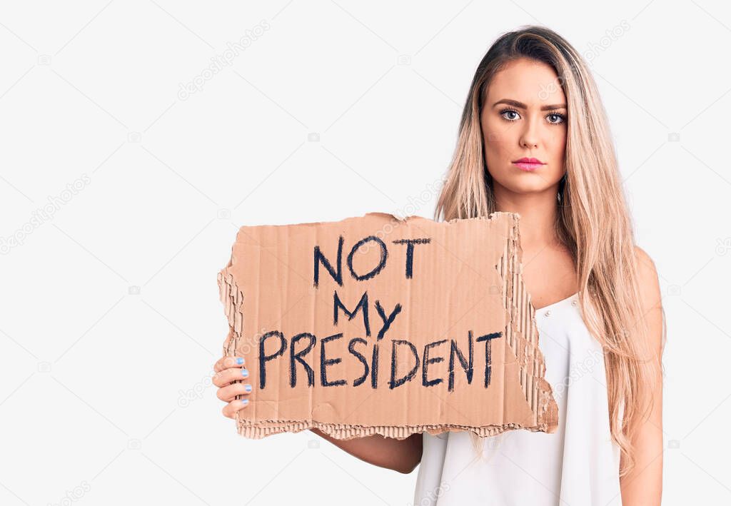 Young beautiful blonde woman holding not my president cardboard banner thinking attitude and sober expression looking self confident 