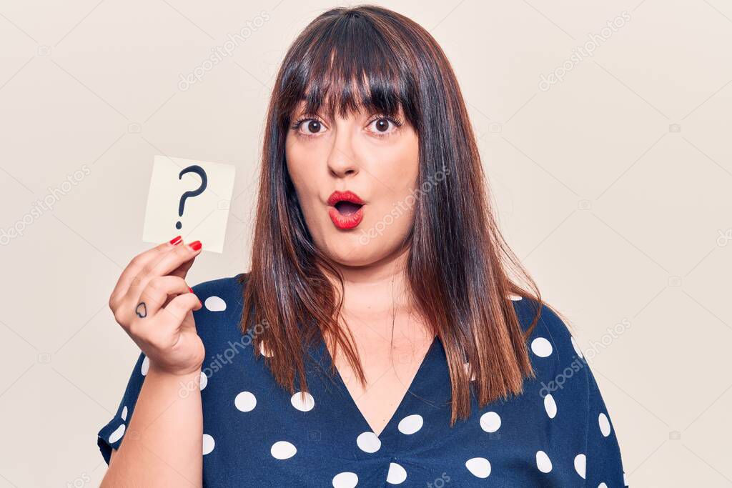 Young plus size woman holding question mark scared and amazed with open mouth for surprise, disbelief face 
