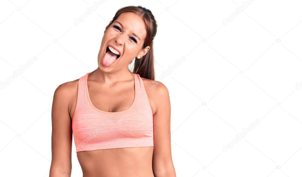 Young beautiful hispanic woman wearing sportswear sticking tongue out happy with funny expression. emotion concept. 