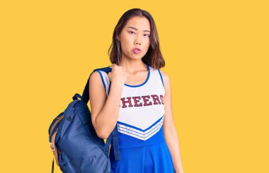 Genç, güzel Çinli kız amigo kız üniforması giyiyor. Sırt çantası taşıyor. Düşünme tavrı takınıyor. 