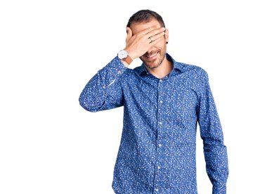 Gündelik kıyafetler giyen, gülümseyen ve gülümseyen genç yakışıklı adam şaşırmak için gözlerini kapatıyor. kör kavram. 