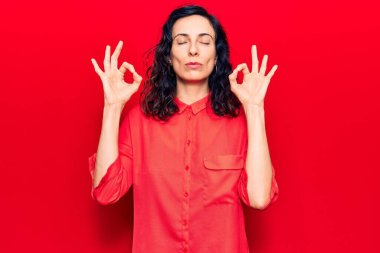 Genç ve güzel İspanyol kadın günlük kıyafetler giyip rahatlıyor ve gözleri kapalı gülümsüyor parmaklarıyla meditasyon hareketi yapıyor. yoga konsepti. 