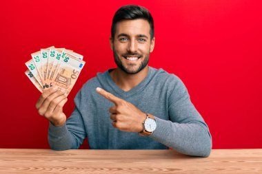 50 Euro 'luk banknotları tutan yakışıklı İspanyol adam mutlu bir şekilde elini ve parmağını gösterdi. 