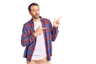 Gündelik kıyafetler giymiş genç yakışıklı bir adam iki eliyle endişeli ve endişeli bir ifadeye işaret ediyor. 