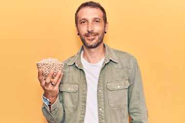 Genç yakışıklı adam elinde nohut kasesi tutarken pozitif ve mutlu görünüyor ve gülümsüyor kendine güvenen bir gülümsemeyle dişlerini gösteriyor. 
