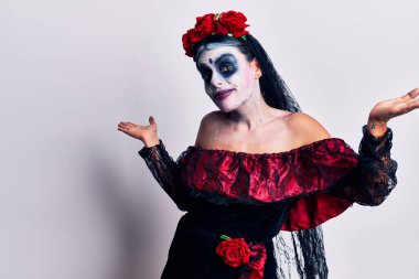 Ölü makyajının Meksika gününü yaşayan genç bir kadın. Kolları ve elleri havada, kafası karışmış bir ifade. şüphe kavramı. 