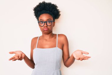 Sıradan kıyafetler giyen, gözlüklü, kafası karışmış, elleri ve kolları havada genç Afrikalı Amerikalı bir kadın. şüphe kavramı. 