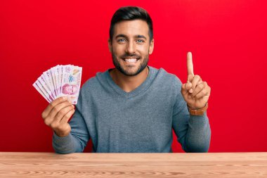 Meksika pesolarını elinde tutan yakışıklı İspanyol bir adam bir fikir veya soruyla gülümsüyor ve mutlu bir yüzle işaret ediyor. 