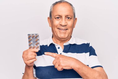 Yaşlı adam elinde haplarla gülümsüyor. El ve parmağıyla mutlu mesut işaret ediyor. 