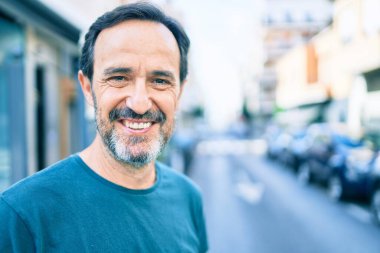 Orta yaşlı, sakallı, açık havada mutlu gülümseyen bir adam.