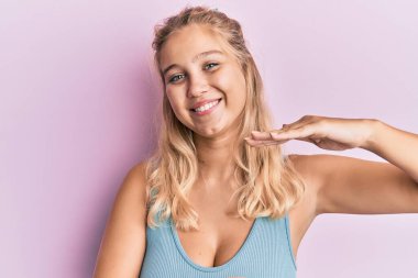 Genç sarışın kız, sıradan kıyafetler giyiyor. Elleriyle işaret ediyor. Büyük ve büyük beden işareti, ölçü işareti. Kameraya bakıp gülümsüyor. ölçüm kavramı. 
