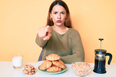 Genç esmer kadın, masada oturmuş kahvaltısını yapıyor. Parmağıyla kamerayı işaret ediyor. Kendine güveni tam bir jest. 