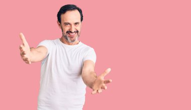 Orta yaşlı, yakışıklı, sıradan tişörtler giyen, gülümseyen, yardım eli uzatan ve kabul gören bir adam.. 