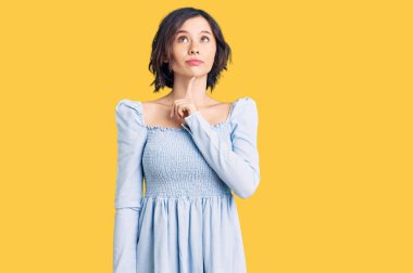 Genç ve güzel bir kız günlük kıyafetler giyip şüpheye odaklanmış, parmakları çenesinde ve yukarı bakıp merak ediyor. 