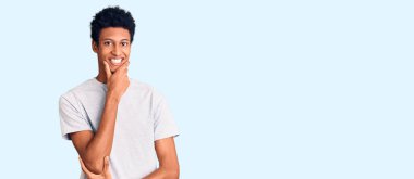 Sıradan kıyafetler giyen genç Afro-Amerikalı adam kameraya kendinden emin bakıyor kollarını kavuşturmuş ve çenesini kaldırmış gülümsüyor. Olumlu düşünmek. 