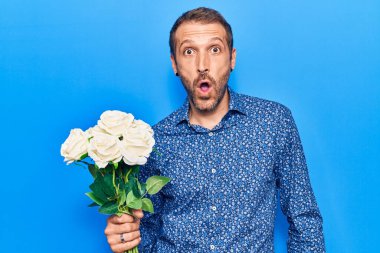 Çiçekleri tutan genç yakışıklı adam korkmuş ve ağzı açık kalmış, şaşırmış ve şaşırmış. 