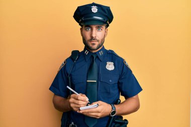 Handsome hispanic man wearing police uniform writing traffic fine relaxed with serious expression on face. simple and natural looking at the camera.  clipart