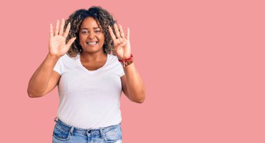 Genç Afro-Amerikan artı cüsseli kadın günlük kıyafetler giyip dokuz numaralı parmaklarıyla işaret ederken kendinden emin ve mutlu bir şekilde gülümsüyor.. 