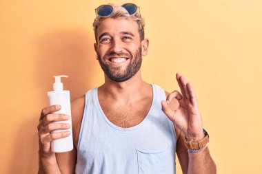 Tatilde sakallı yakışıklı sarışın bir adam tenini korumak için bir şişe güneş kremi tutuyor.