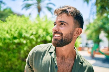 Parkta yürürken gülümseyen İspanyol genç adam.