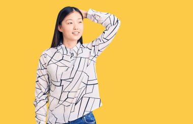 Genç, güzel, Çinli bir kadın, rahat bir tişört giyiyor, gülümsüyor, kendine güveniyor, saçlara dokunuyor, el hareketi yapıyor, çekici ve modaya uygun poz veriyor. 