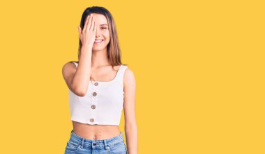 Kolsuz tişört giyen genç güzel bir kız bir gözünü eliyle kapatıyor, yüzünde kendine güvenen bir gülümseme ve sürpriz bir duygu var.. 