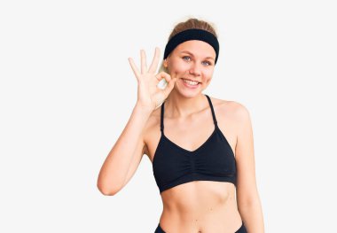 Spor kıyafetleri giyen genç ve güzel sarışın kadın gülümsüyor ve el ve parmaklarıyla 