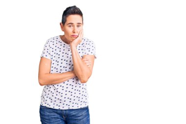 Kısa saçlı, günlük kıyafetler giyen, yorgun görünen ve depresyondan sıkılmış kollarını kavuşturmuş genç bir kadın.. 