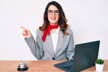 Otel resepsiyonunda çalışan genç, güzel esmer kadın dizüstü bilgisayarını kullanarak mutlu bir şekilde gülümsüyor. 