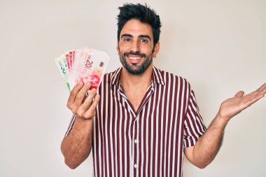 Sakallı yakışıklı İspanyol adam İsrail şekelleri tutuyor başarıyı mutlu bir gülümsemeyle kutluyor ve kazanan el kaldırarak ifade ediyor 