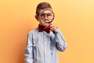 Sevimli sarışın çocuk inek papyonu takıyor ve gözlük takıyor. Büyüteç takıyor. Düşünme tavrı takınıyor. 